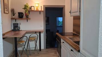 Una cucina compatta con un tavolo di legno, due sedie, una moka e un frigorifero.