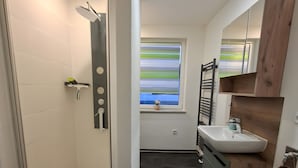 A modern bathroom with a shower, sink, and window.