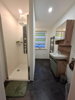 A modern bathroom with a shower, sink, and window. - Apartment “John” with Private Garden (Geratal)