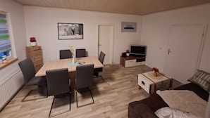 A living room with a wooden dining table, chairs, a TV, a sofa, and a small cabinet.
