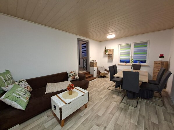 A living room with a brown sofa, a white coffee table, and a dining area with a table and chairs.