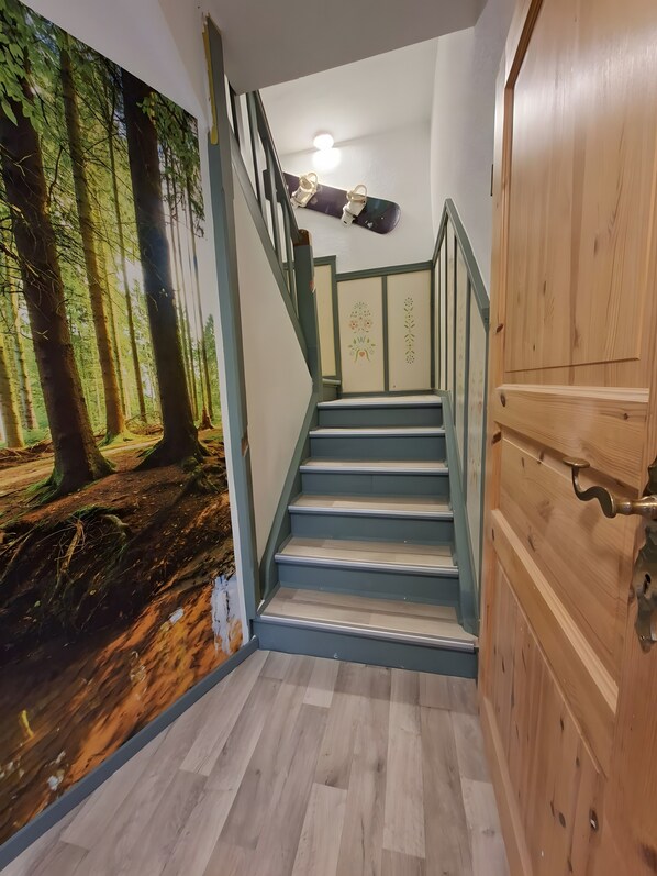 A staircase with a forest mural on the wall, a light fixture above, and a wooden door to the right.
