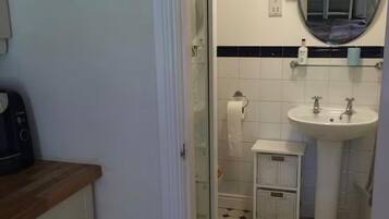 Ein Badezimmer mit einem weißen Waschbecken, einem Spiegel und einer Toilette. Ein kleiner, weißer Schrank mit Schubladen ist ebenfalls vorhanden. Der Boden ist mit einem schwarz-weißen Fliesenspiegel versehen.