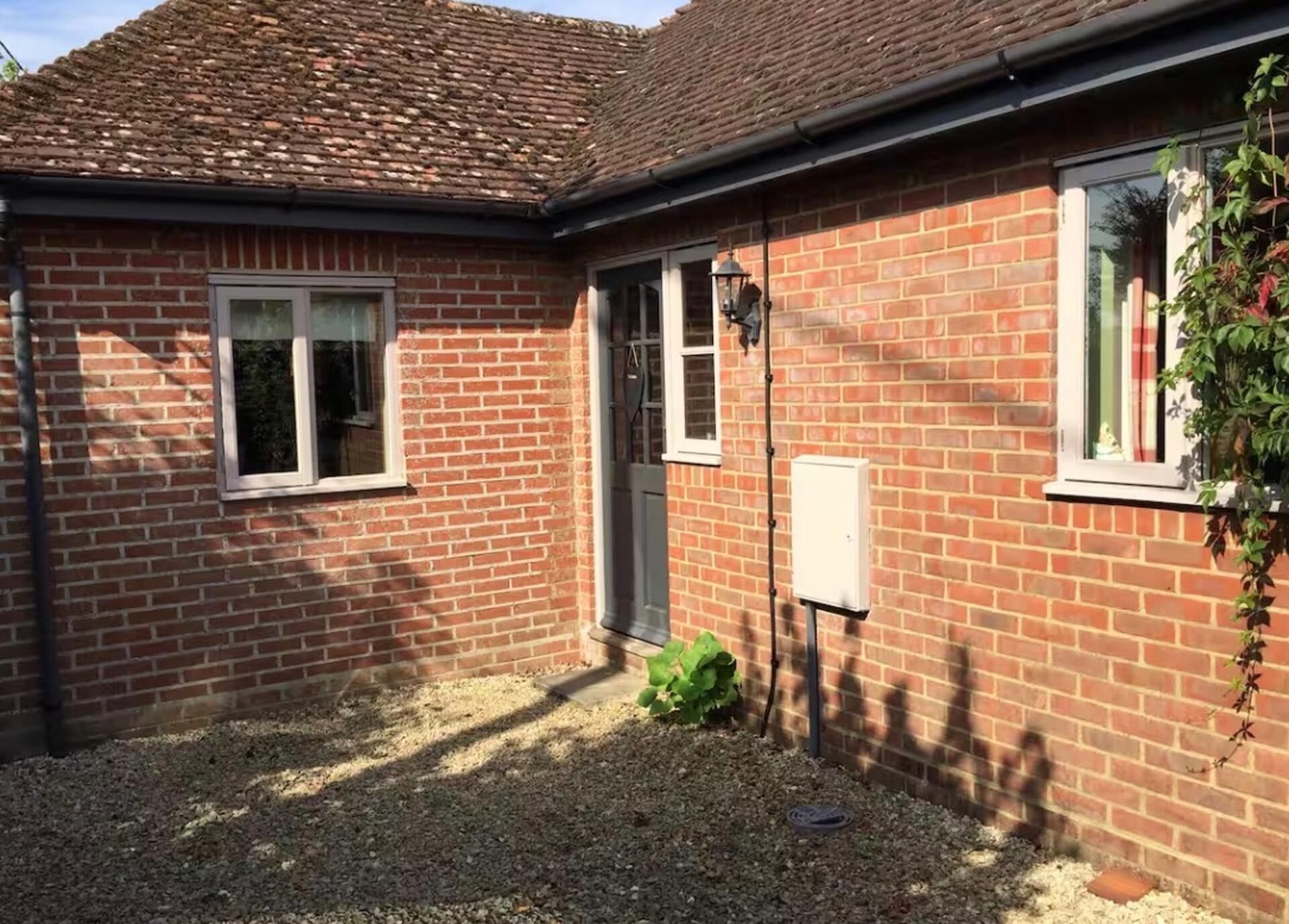 Ein Ziegelhaus mit einem Ziegeldach, ein kleiner Garten mit Kies und ein Fenster mit einer Pflanze daneben.