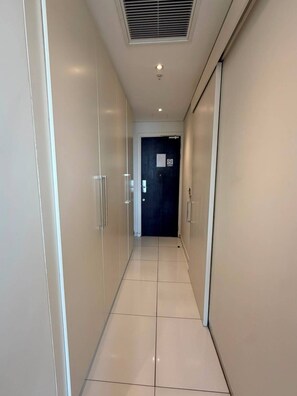 Ein Korridor mit einer Tür am Ende, einem Lüftungsgitter an der Decke und einem gefliesten Boden.