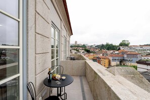 A balcony with a table and chairs, overlooking a cityscape with buildings and a distant tower. - Stylish Flat Near the Douro River by HostWise (Vila Nova de Gaia)