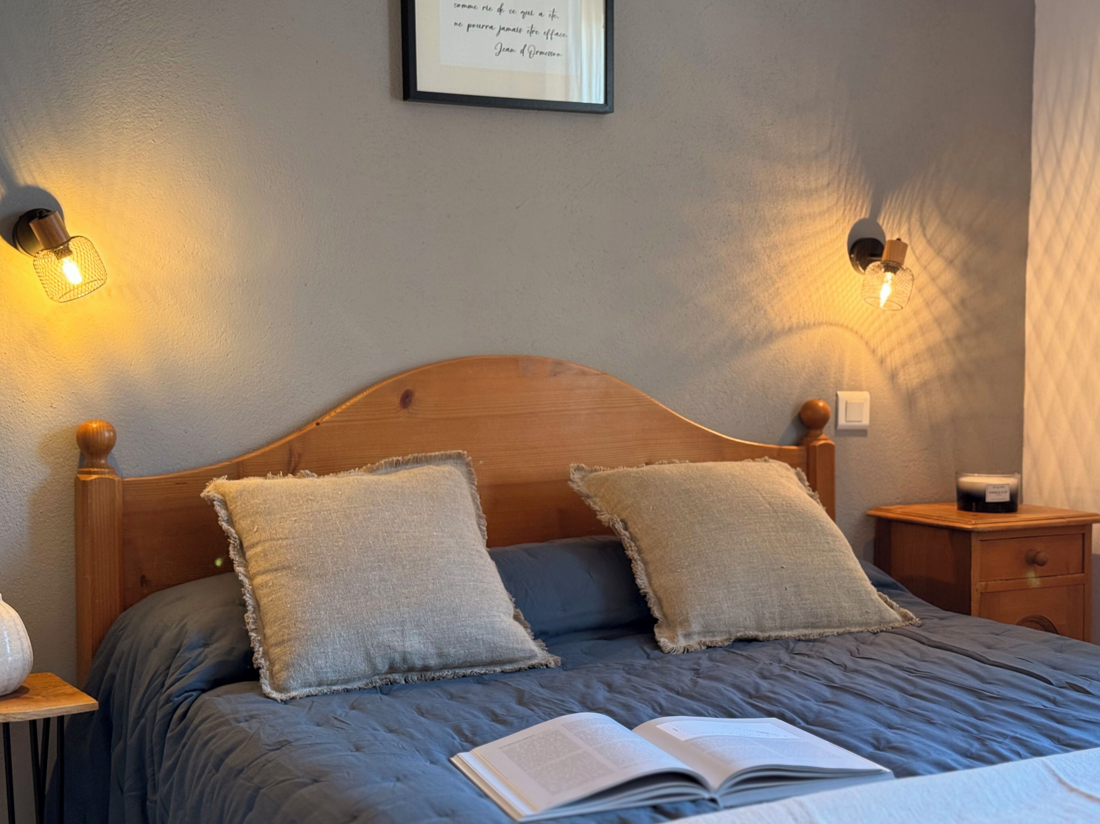 A neatly made bed with two pillows, a bedside table with a lamp, and a framed quote on the wall.