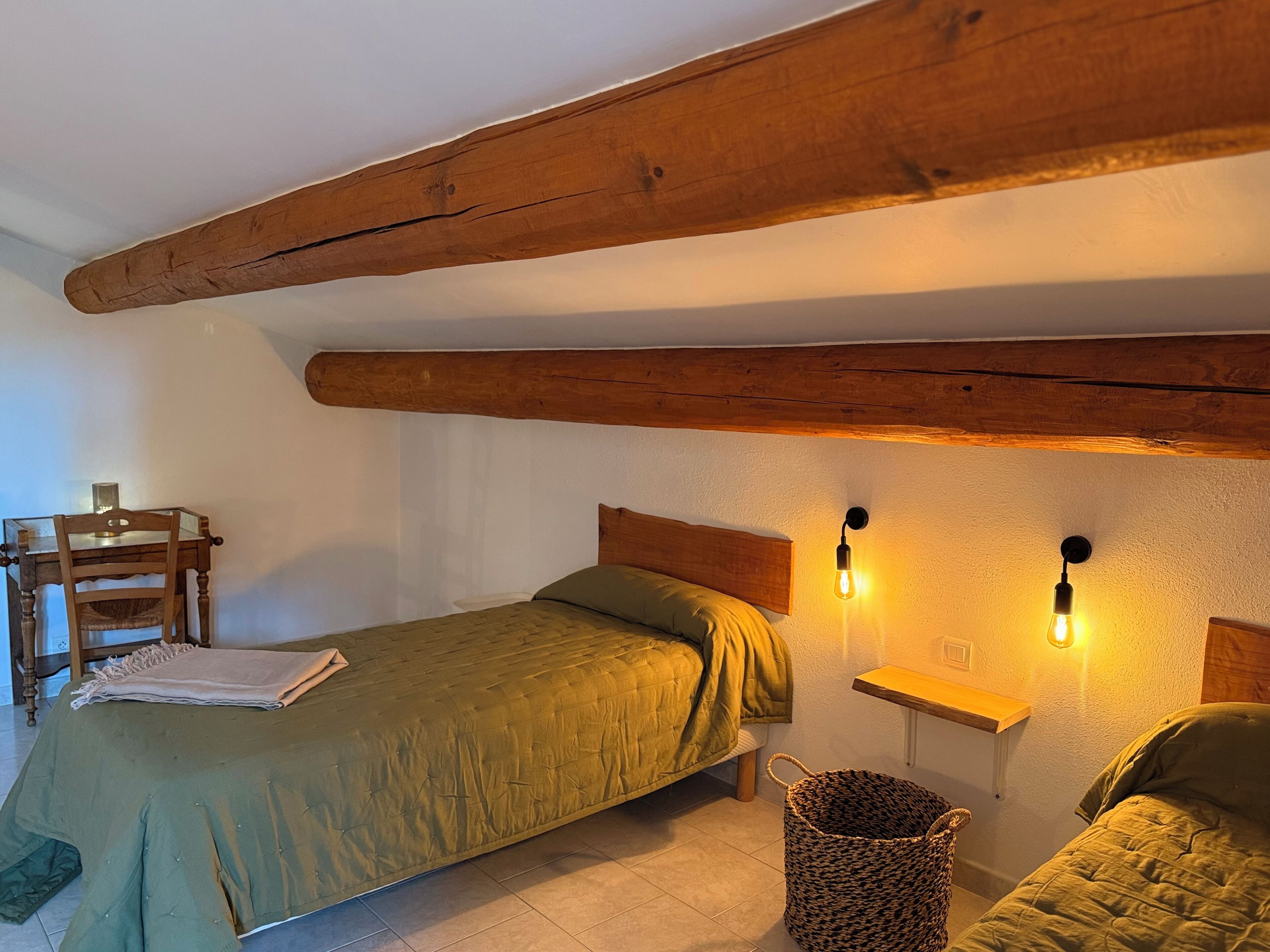 Una stanza con un letto, una sedia, un tavolino e una lampada a parete.
