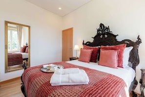 Ein Hotelzimmer mit einem großen Bett, einem Holz-Kopfende, einem Spiegel, einem Nachttisch mit Lampe und einem Fenster mit Vorhängen.
