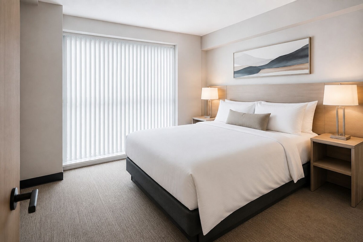 Ein Hotelzimmer mit einem großen Bett, zwei Nachttischen mit Lampen, einem Fenster mit Jalousien und einem Bild an der Wand.