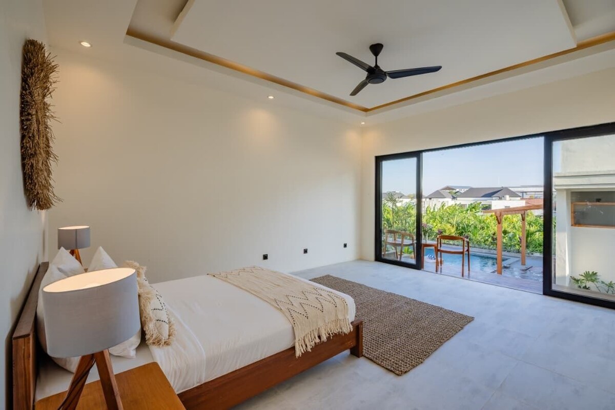 Una camera da letto con un letto, una ventola a soffitto, un'ampia finestra e vista sull'esterno.