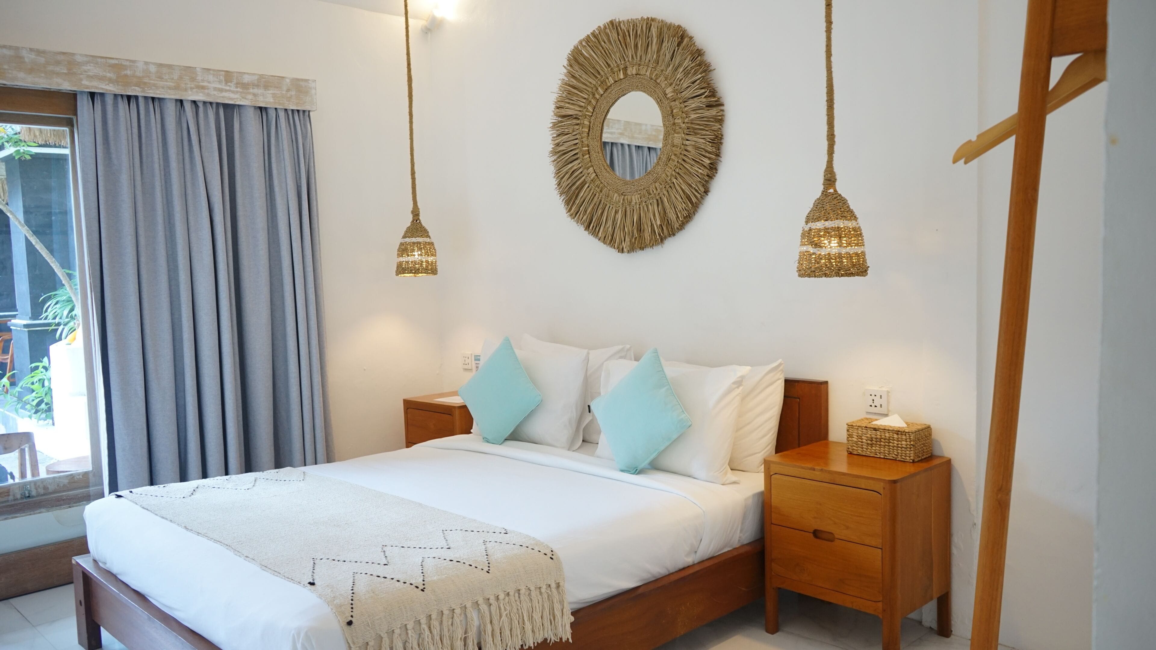 A bedroom with a large bed, two bedside tables, a hanging mirror, and two pendant lights.