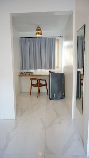 A compact room with a desk, chair, and a refrigerator. - Wanderlust Hotel (Tibubeneng)
