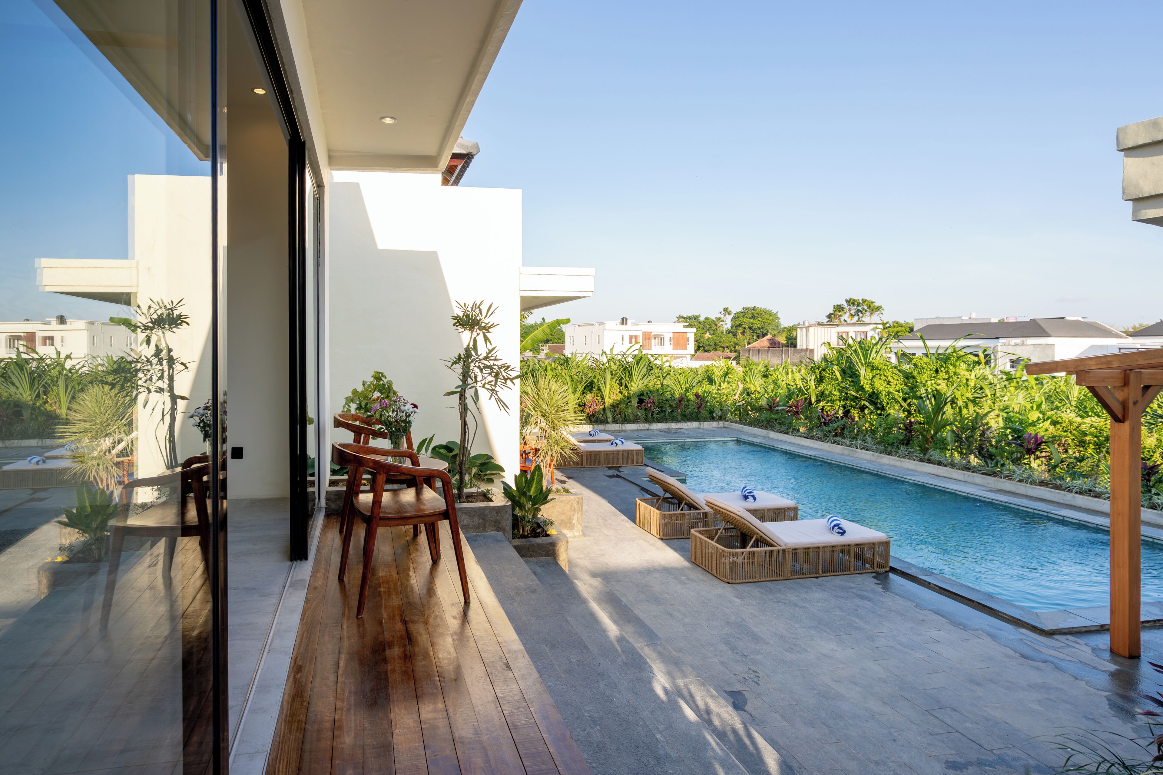 Un área de piscina exterior moderna con sillones reclinables y una mesa de comedor.