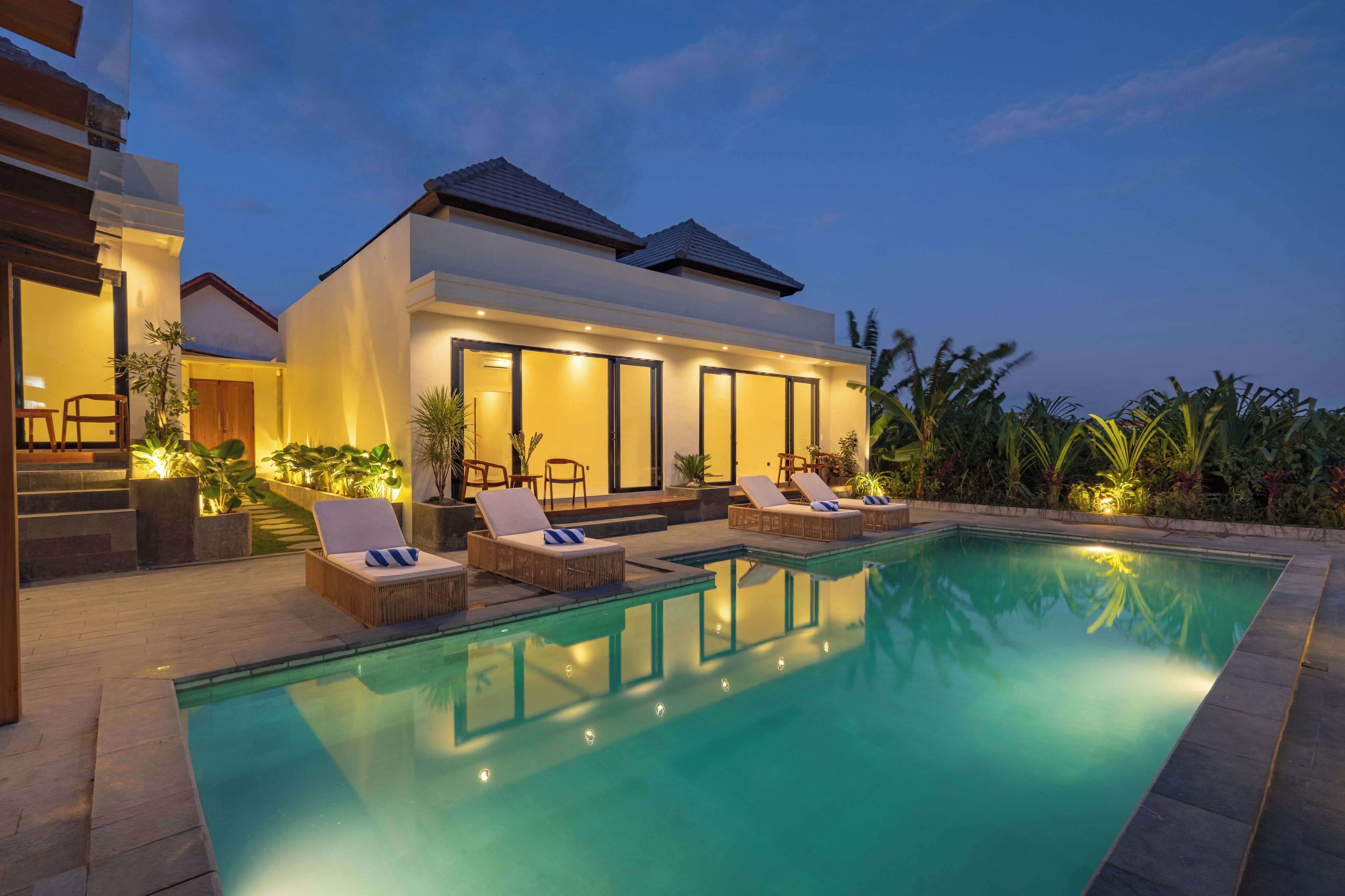 Una casa moderna con piscina, sillas de descanso y un exterior bien iluminado.