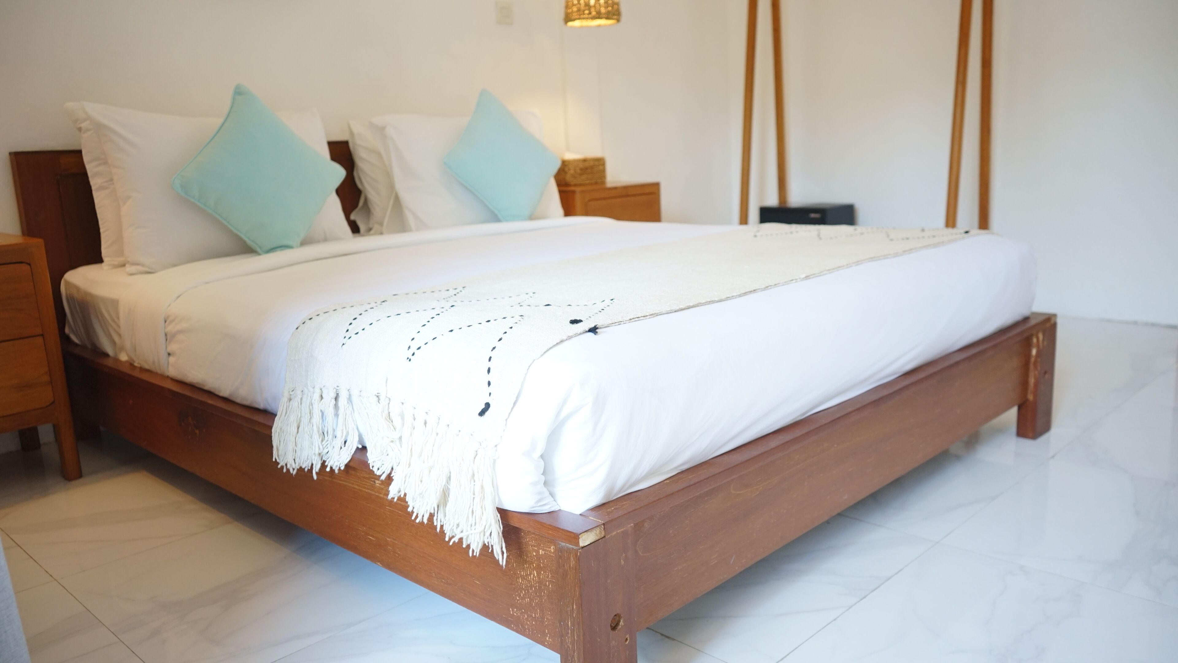 Una cama de madera con ropa de cama blanca y almohadas azules en una habitación con suelo de baldosas.