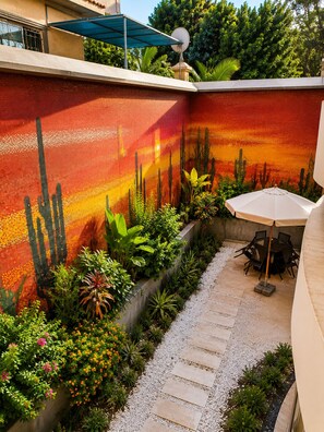Un cortile con un giardino di cactus, un'area salotto con tavolo e sedie, e un vialetto sterrato.