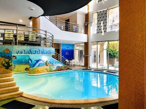 Una piscina interna con un murale di delfini, una scala e vista sull'esterno.