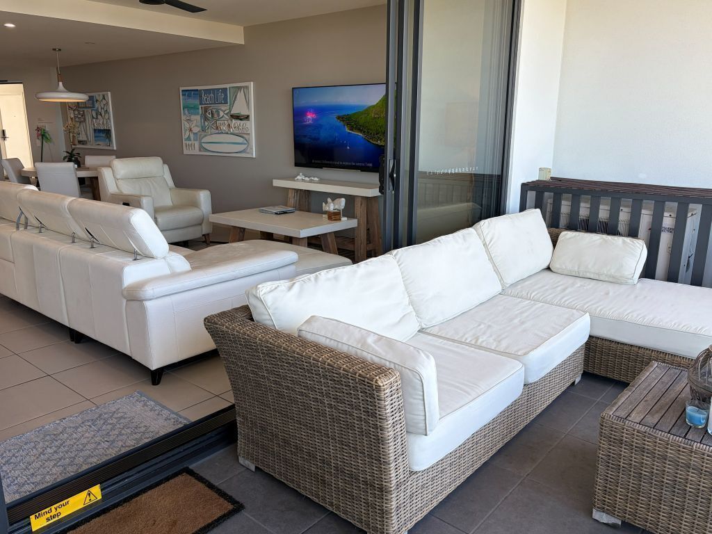 Un salon moderne avec un canapé blanc, un élément décoratif en osier et un téléviseur à écran plat posé sur un meuble.