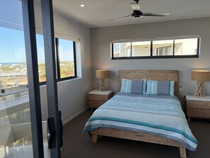 Ein Schlafzimmer mit einem großen Bett, zwei Nachttischen, einem Deckenventilator und einem Fenster mit Blick auf Gebäude.