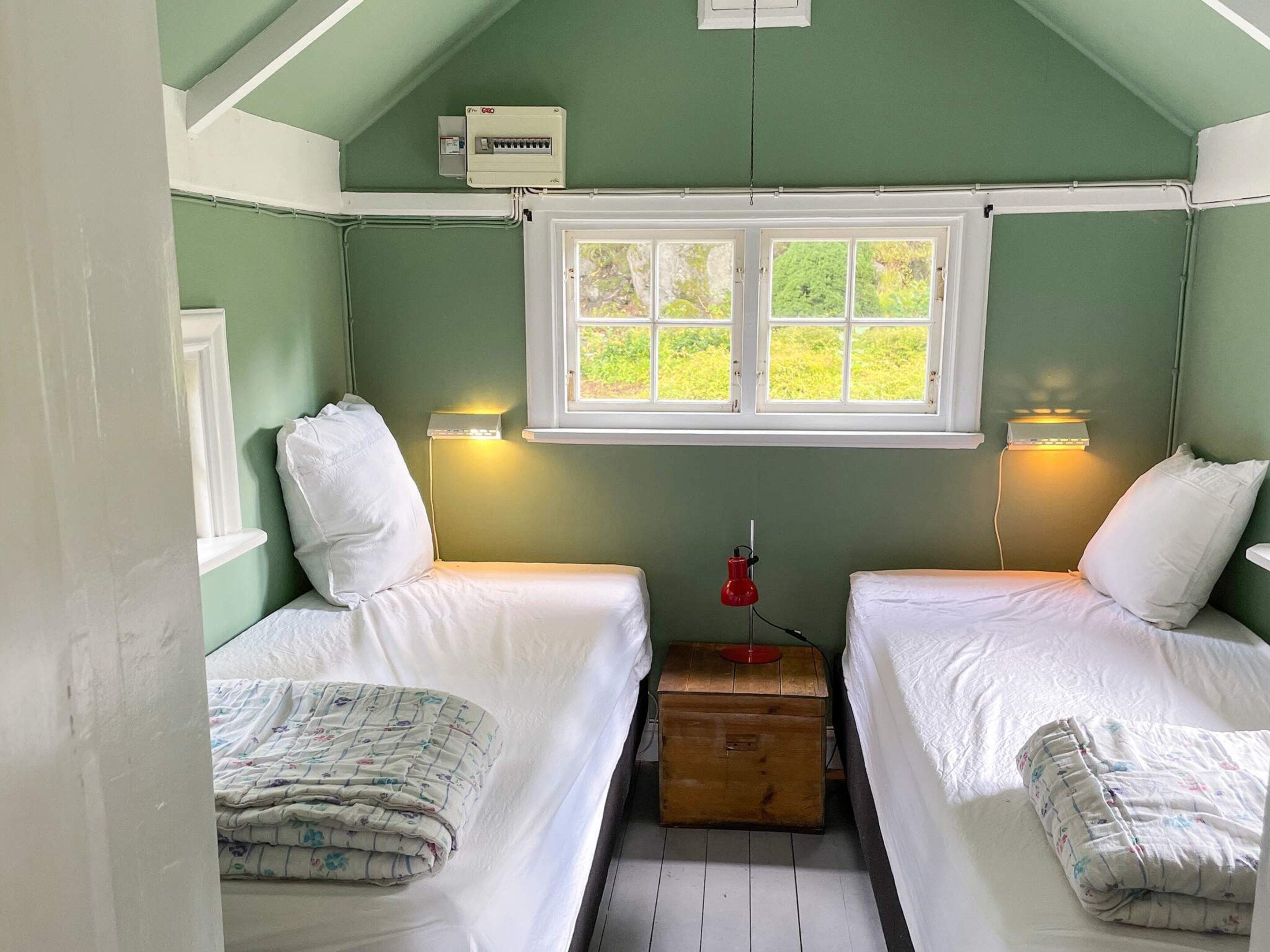 A small, cozy room with two beds, a window, and a wooden chest.