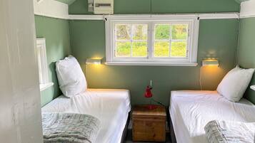 A small, cozy room with two beds, a window, and a wooden chest.