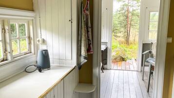 Una habitación con ventana, hervidor, silla y puerta que da a un espacio exterior.