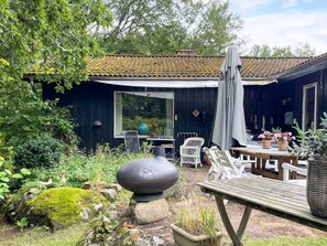 A rustic outdoor seating area with a wooden table and chairs, a large decorative stone, and a covered patio with a tiled roof. - 5 Star Holiday Home in Knared (Knared)