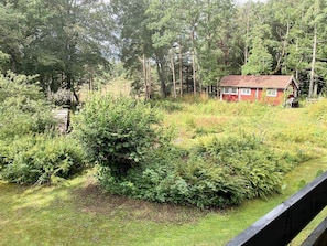 Een rode blokhut, omringd door een dicht bos en een grasveld.
