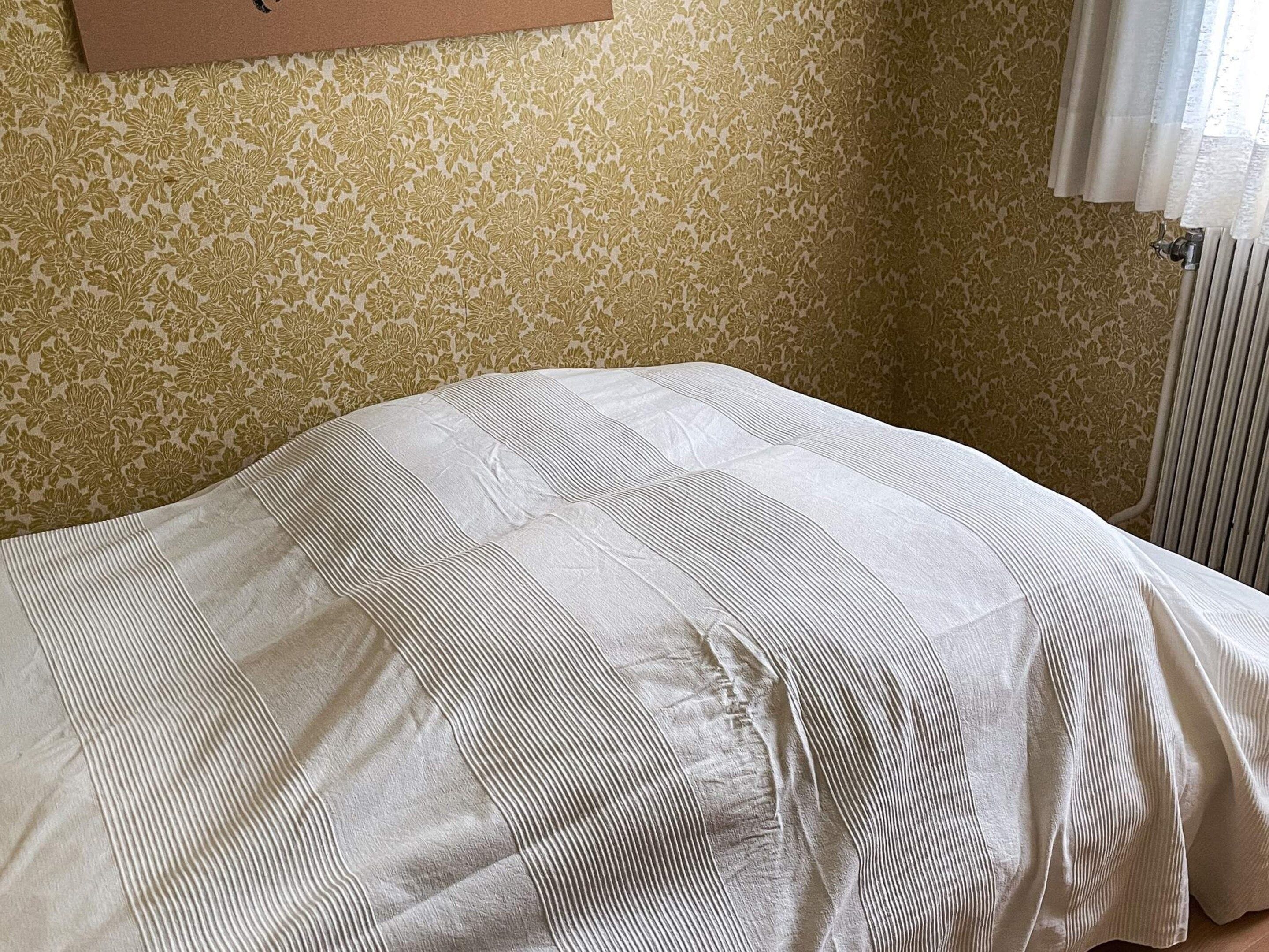 A bed with a striped blanket in a room with patterned wallpaper.