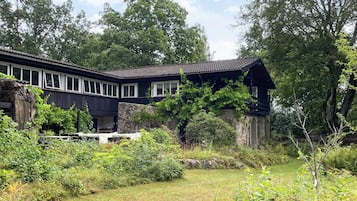 A two-story house with a stone foundation, surrounded by lush greenery and trees.