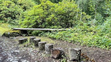 A stone pathway leading through a garden with a wooden bench and tree stumps.