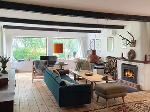 Una sala de estar acogedora con chimenea, suelo de madera y un gran ventanal con vistas a la vegetación.