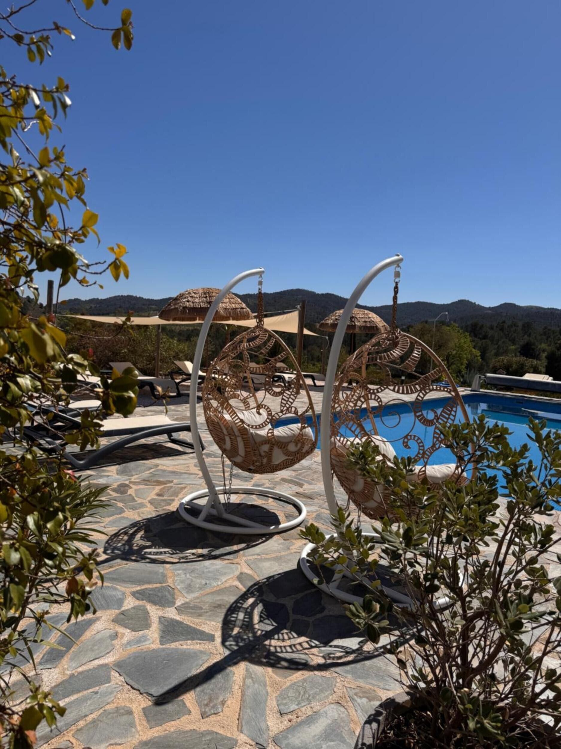 Zona de piscina con suelo de piedra, sillones de mimbre y vistas despejadas a las montañas.