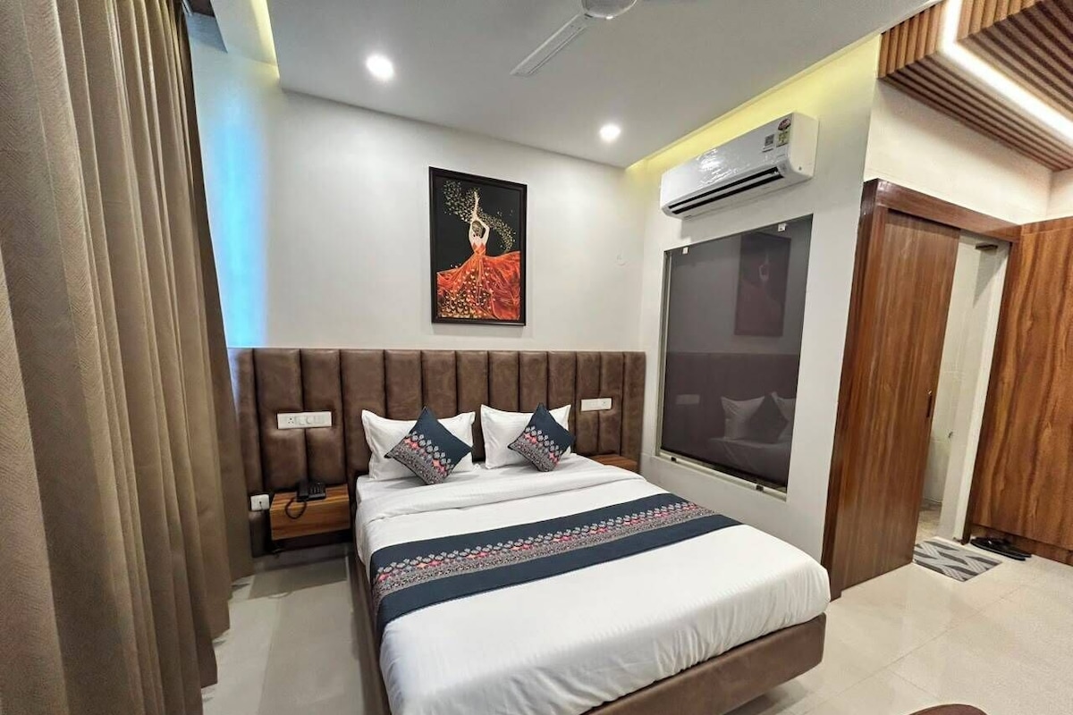 A modern hotel room with a bed, a nightstand, a window, and an air conditioning unit.