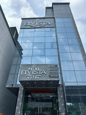 The exterior of the Prime Elvista Hotel with a modern glass facade, a prominent sign, and a welcome sign at the entrance. - Hotel Prime Elvista  (Zirakpur)