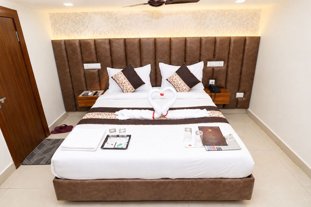 Una habitación de hotel con una cama grande, cabecera, mesitas de noche, una puerta y un ventilador de techo.