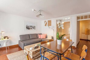 A modern living room with a grey sofa, wooden coffee table, and a dining area with a wooden table and chairs. - Oak Valley Flats, Bairro Alto—2 minutes from Chiado (Lisboa)