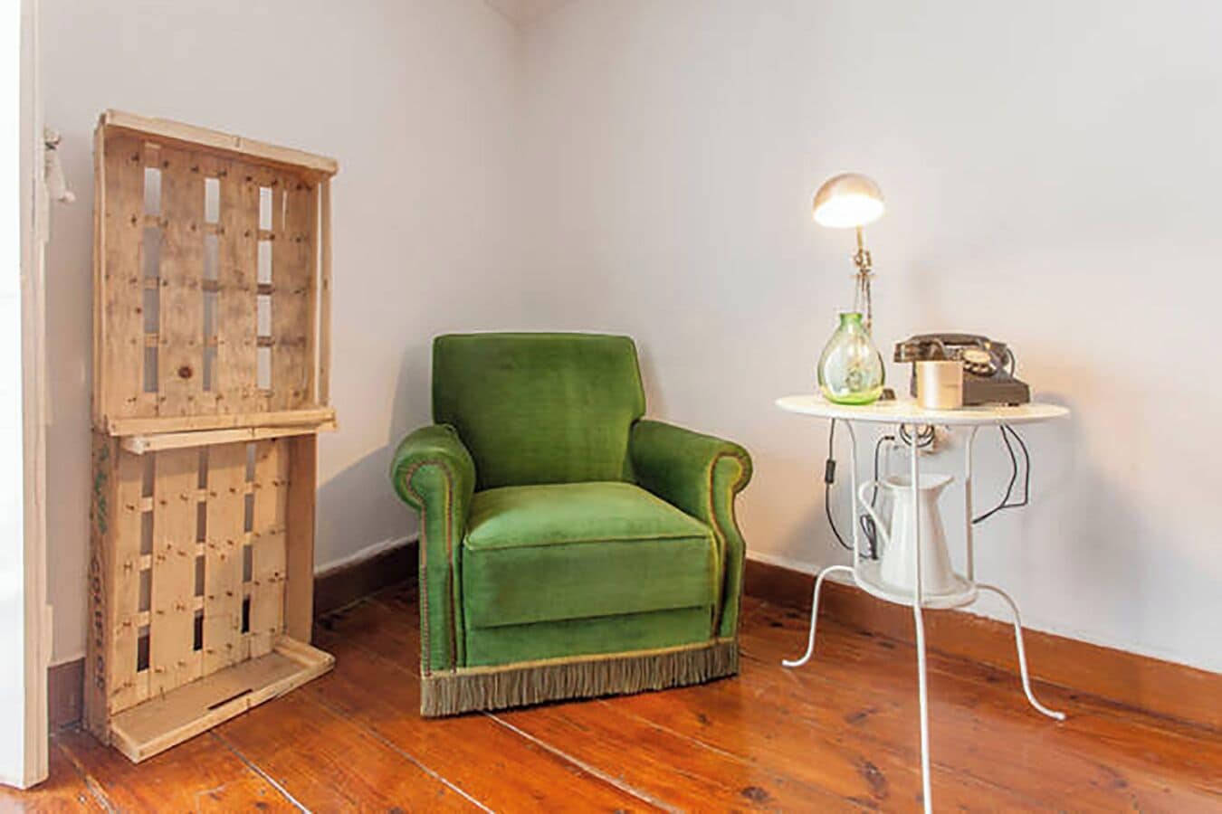 A room with a green armchair, a wooden crate, and a small table with a lamp and a vintage radio.
