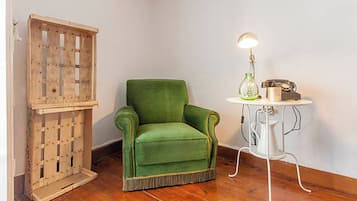 A room with a green armchair, a wooden crate, and a small table with a lamp and a vintage radio.