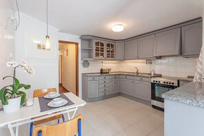 A compact kitchen with grey cabinets, a stove, and a dining area with a table and chairs. - Oak Valley Flats, Bairro Alto—2 minutes from Chiado (Lisboa)
