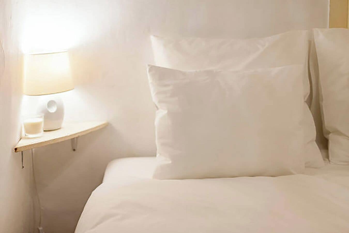 A bed with white bedding and pillows, a bedside table with a lamp and a glass of water.
