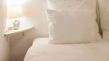 A bed with white bedding and pillows, a bedside table with a lamp and a glass of water.