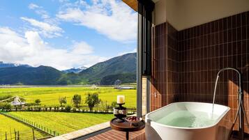 Un baño con bañera y vistas a un campo verde y montañas.