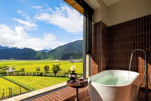 Un baño con bañera y vistas a un campo verde y montañas.