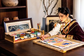 Una persona pinta sobre una tabla de madera con pinturas y pinceles de distintos colores sobre la mesa.