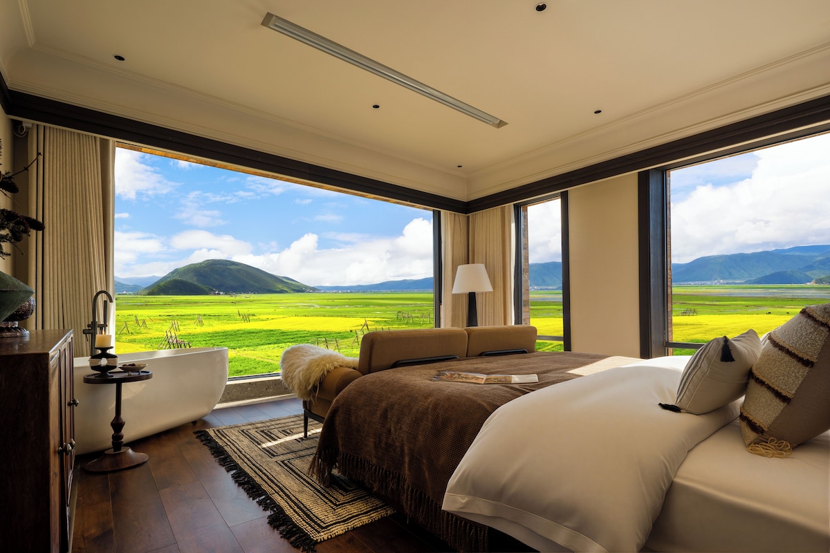 Un dormitorio con una ventana grande, una cama, una mesita de noche y vistas a un paisaje verde.