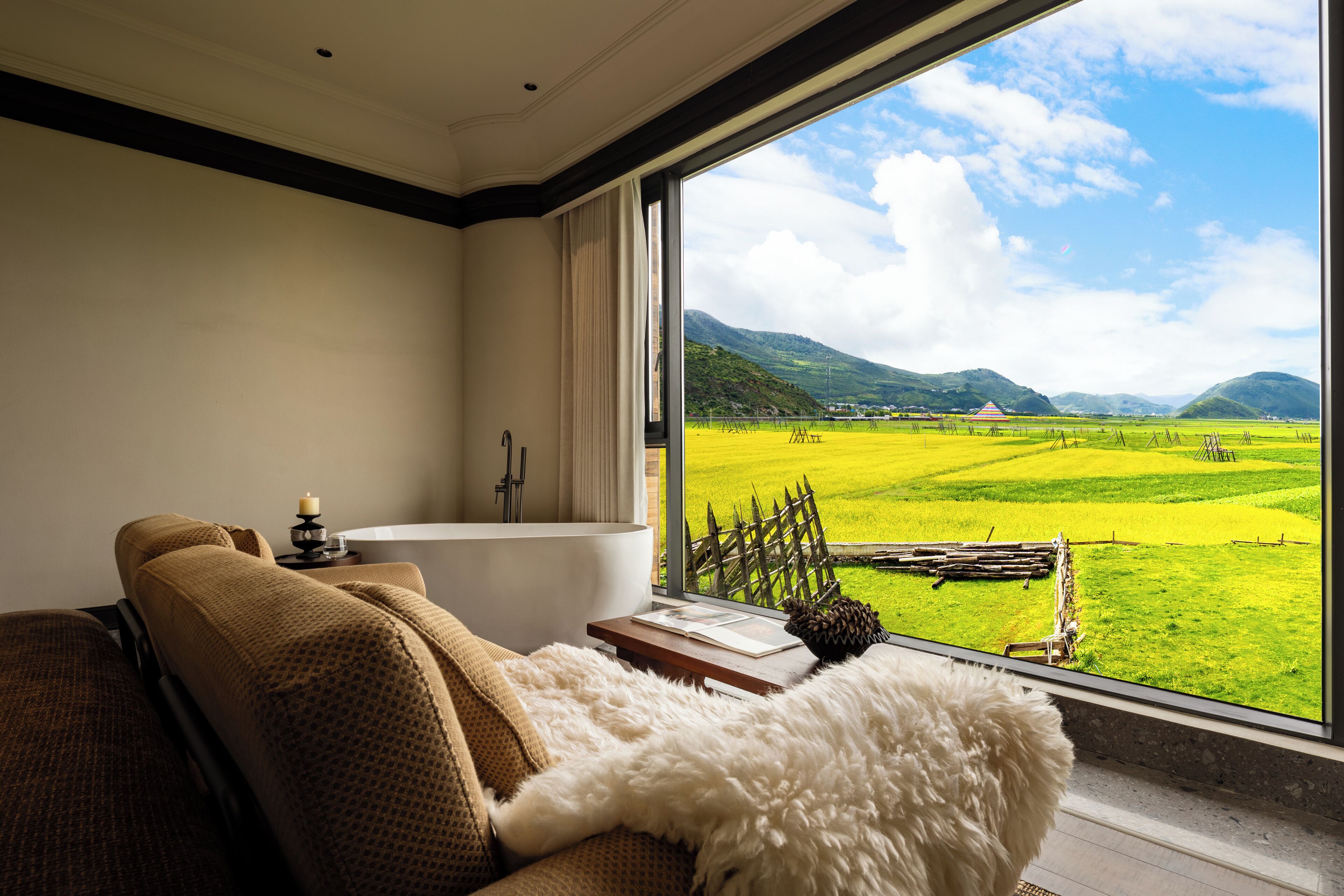 Un baño moderno con bañera, vistas a un campo verde y montañas a través de un ventanal grande.