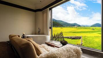 Un bagno moderno con una vasca, vista su un campo verde e montagne attraverso una grande finestra.