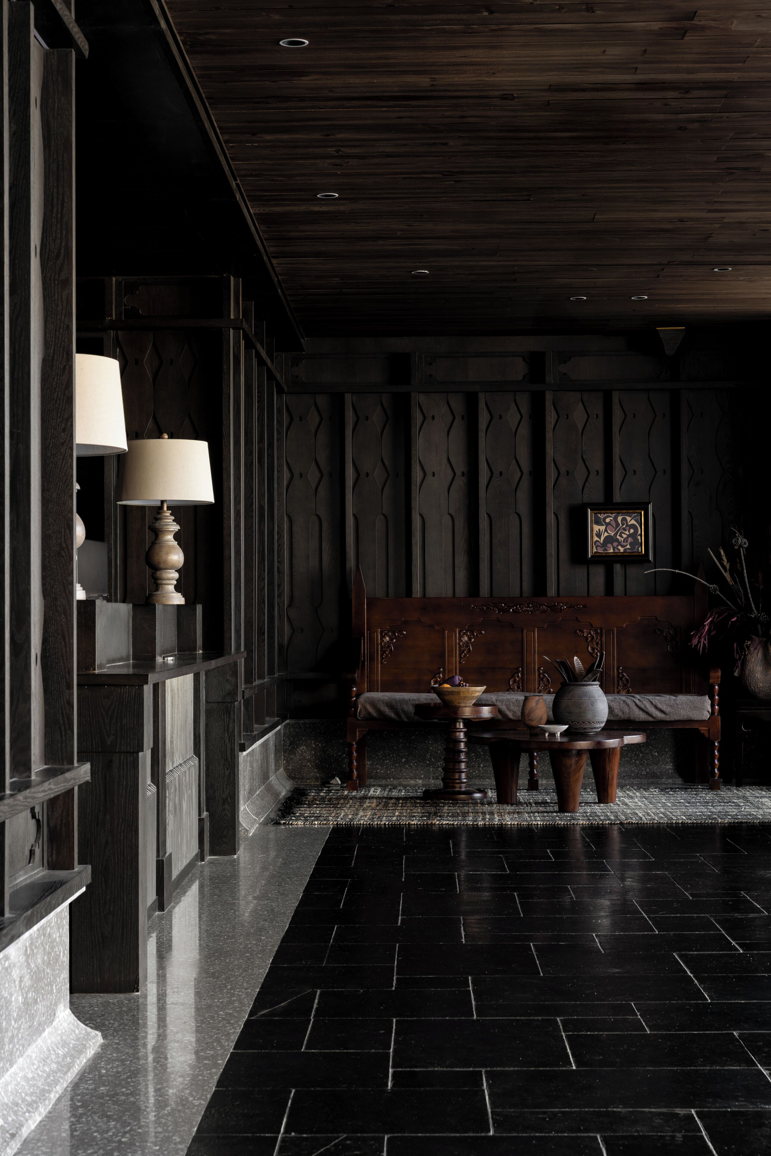 Eine Lobby mit dunklem Holzboden, einer Couch, einem Tisch mit Lampe und einem gerahmten Bild an der Wand.
